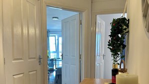 Un pasillo con piso de madera, puertas blancas, una mesa de comedor con velas y una planta colgante.