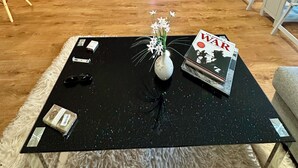 Una sala de estar moderna con una mesa de centro negra, un jarrón con flores, una revista y un televisor.
