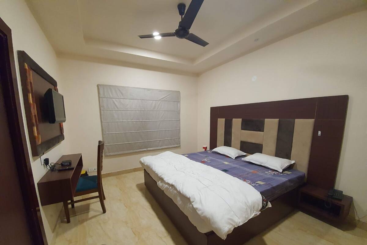 Un dormitorio con cama, escritorio, silla, televisor y ventilador de techo.