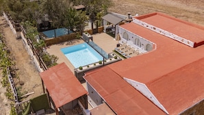 Ein großer Pool im Freien mit Sonnenterrasse, umgeben von einer Hecke mit Bäumen und Blick auf eine Wüstenlandschaft.