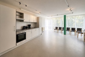 Una cocina moderna con gabinetes blancos, una estufa y una cafetera. Hay sillas y una mesa en una habitación luminosa con ventanas grandes.