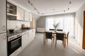 Eine moderne Küche mit weißen Schränken, einem schwarzen Herd und einem Essbereich mit einem Holztisch und Stühlen.