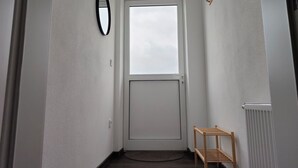 Um corredor estreito com uma porta branca, uma pequena prateleira de madeira e um tapete redondo no chão.