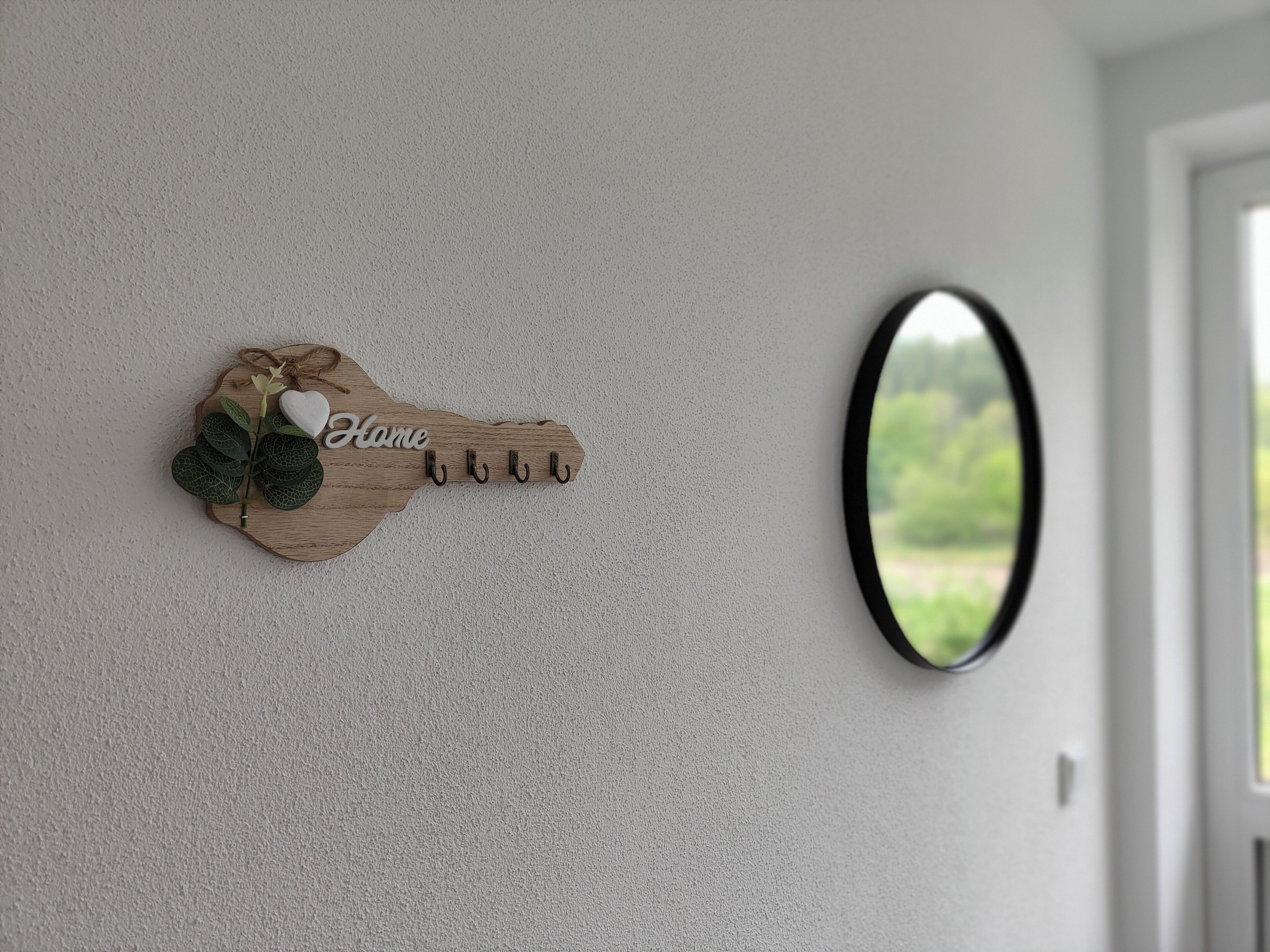 A wall-mounted key hook with a heart-shaped key and the word 'Home' on a textured wall.