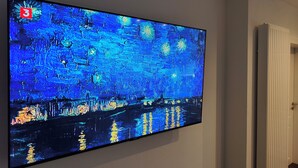 Televisão de tela plana fixada na parede exibindo uma pintura.