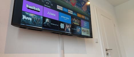 Uma TV de tela plana na parede exibindo a interface de um serviço de streaming com diversas opções.