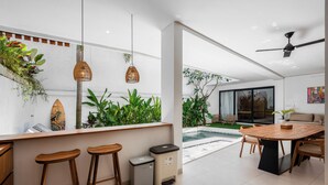 A modern kitchen with a bar area, a dining table, and a view of a pool. - L'Angelo Villa Canggu (Canggu)