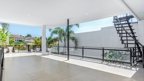 A spacious balcony with a metal staircase, potted plants, and a view of houses in the background. - L'Angelo Villa Canggu (Canggu)