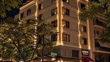 A multi-story hotel with illuminated columns, outdoor seating, and a visible restaurant named 'NIXON Downtown'.