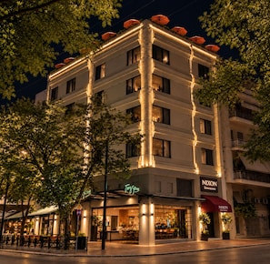 A multi-story hotel with illuminated columns, outdoor seating, and a visible restaurant named 'NIXON Downtown'. - THE NIXON Downtown (Athens)