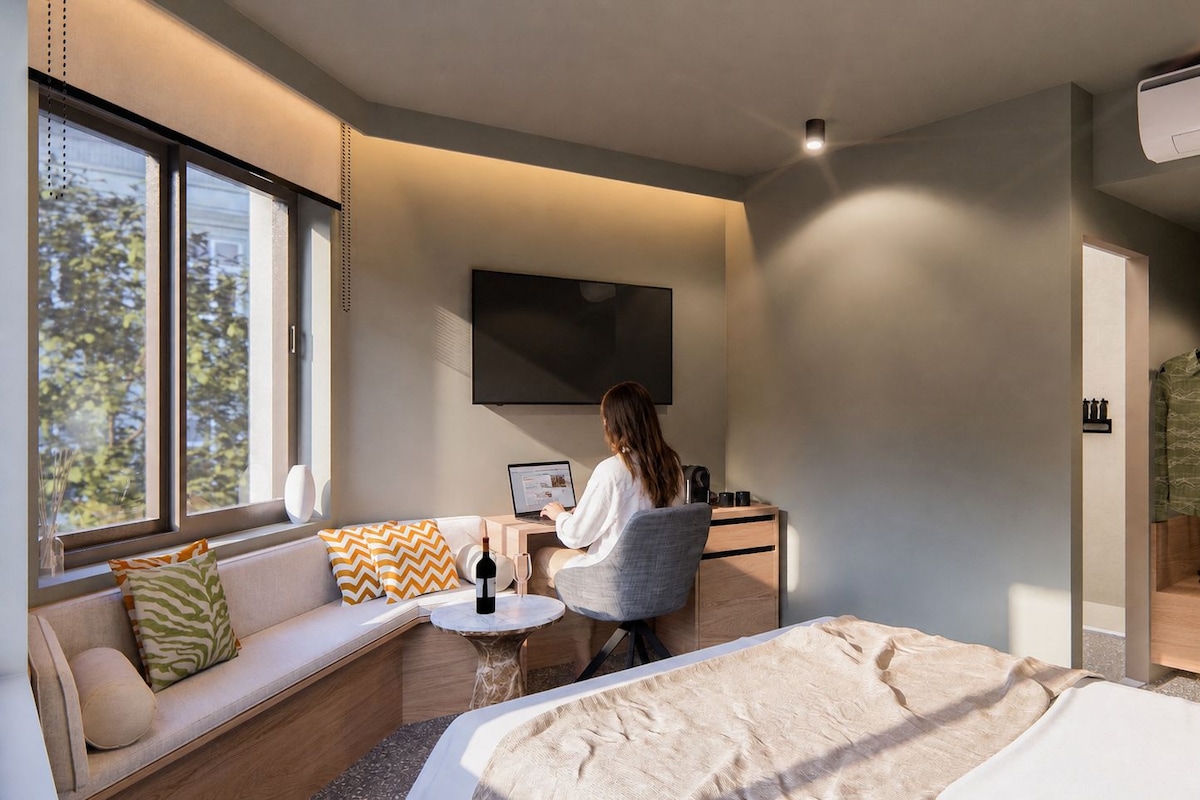 A modern hotel room with a sofa, a desk, a bed, a TV, and a wardrobe.