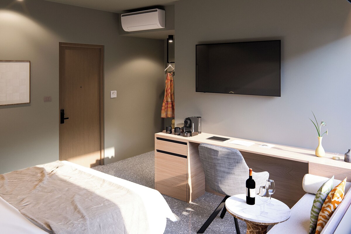 A hotel room with two beds, a desk with a chair, a flat-screen TV, and a small table with a bottle and glass.