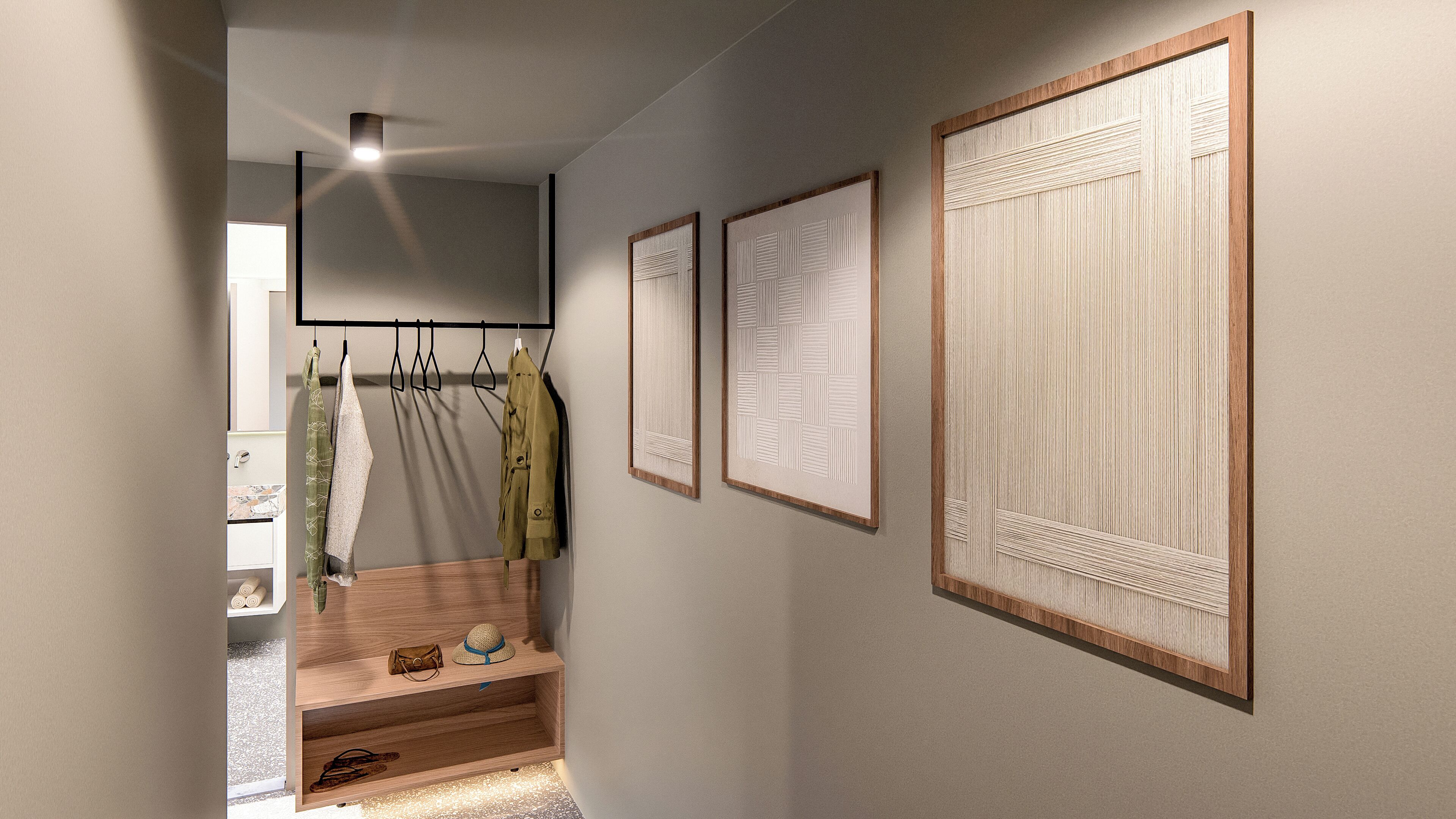 Un couloir avec un banc en bois, un porte-manteau sur lequel sont suspendus des vêtements et des œuvres d’art encadrées accrochées au mur.
