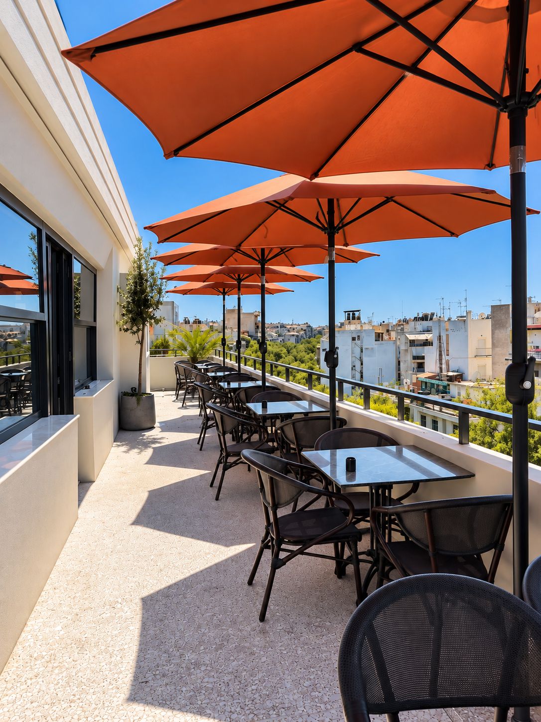 Une terrasse extérieure avec des tables et des chaises, des parasols orange et une vue sur le paysage urbain.