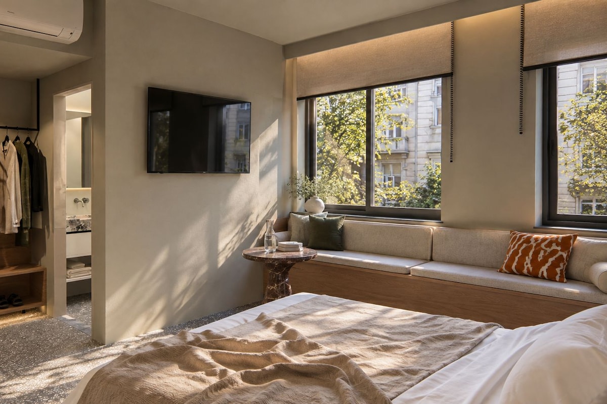 A modern bedroom with a bed, a seating area with a view, a TV, and a wardrobe.