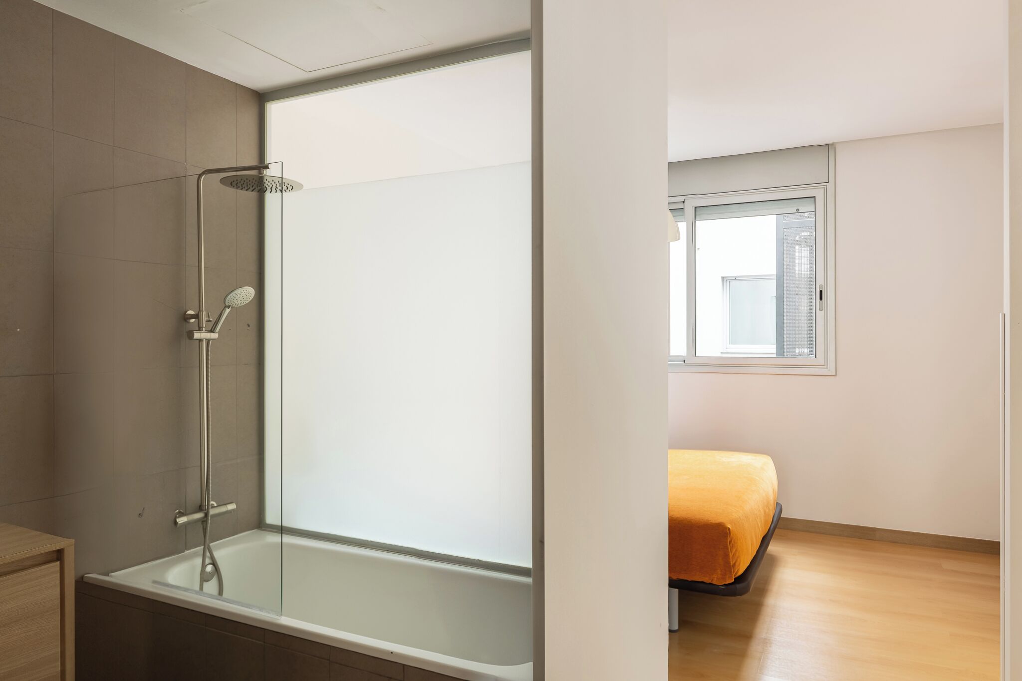 A modern bathroom with a glass shower enclosure, a bathtub, and a wooden floor.