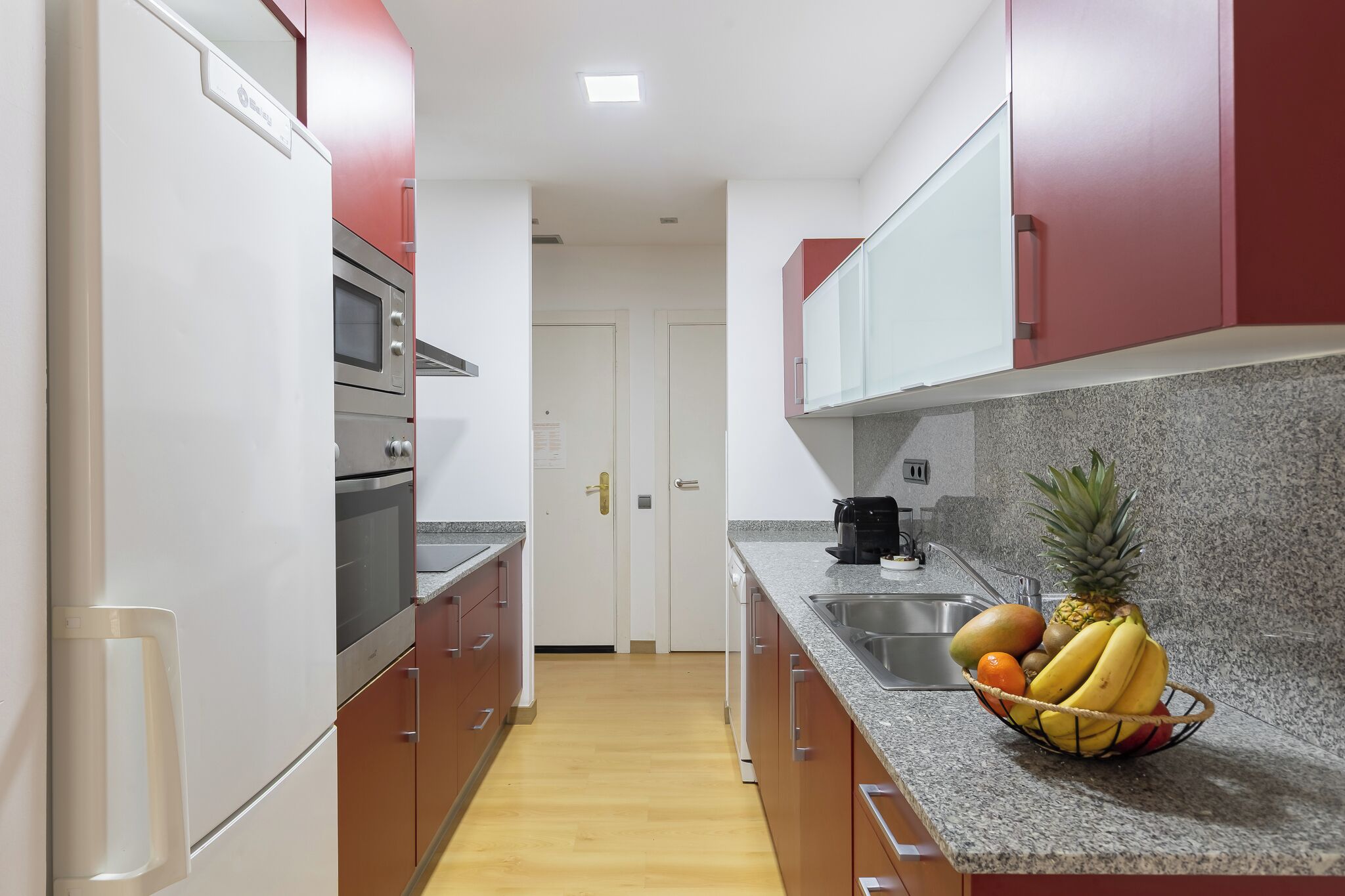 A modern kitchen with stainless steel appliances, granite countertops, and red cabinetry.