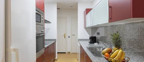 A modern kitchen with stainless steel appliances, granite countertops, and red cabinetry.