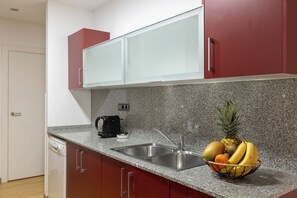 A kitchen with granite countertops, a stainless steel sink, red cabinets, and a fruit bowl. - Cosmo Apartments Casanova (Barcelona)