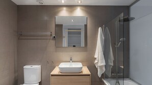 Un baño moderno con inodoro, lavamanos, espejo y ducha.