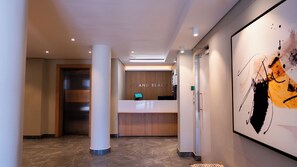 Ein Hotel-Empfangsbereich mit einem Holztresen, einem digitalen Bildschirm und einem Schreibtisch mit der Beschriftung 'STRAND BEACH'.