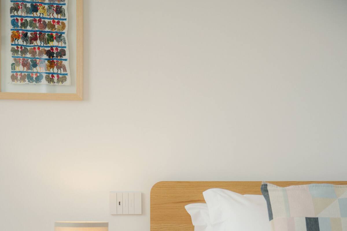 Ein Hotelzimmer mit einem Bett, einem Nachttisch mit Lampe und einem an der Wand montierten Lichtschalter.