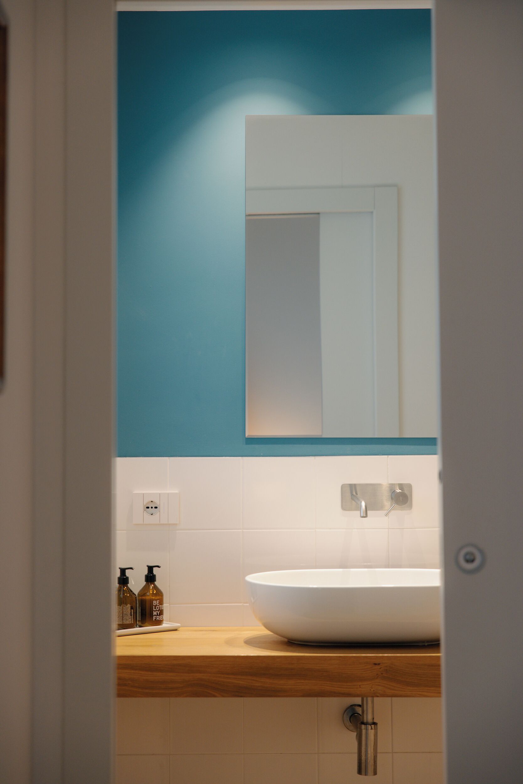 Une salle de bain avec un lavabo blanc, un miroir et un mur d’accent bleu.