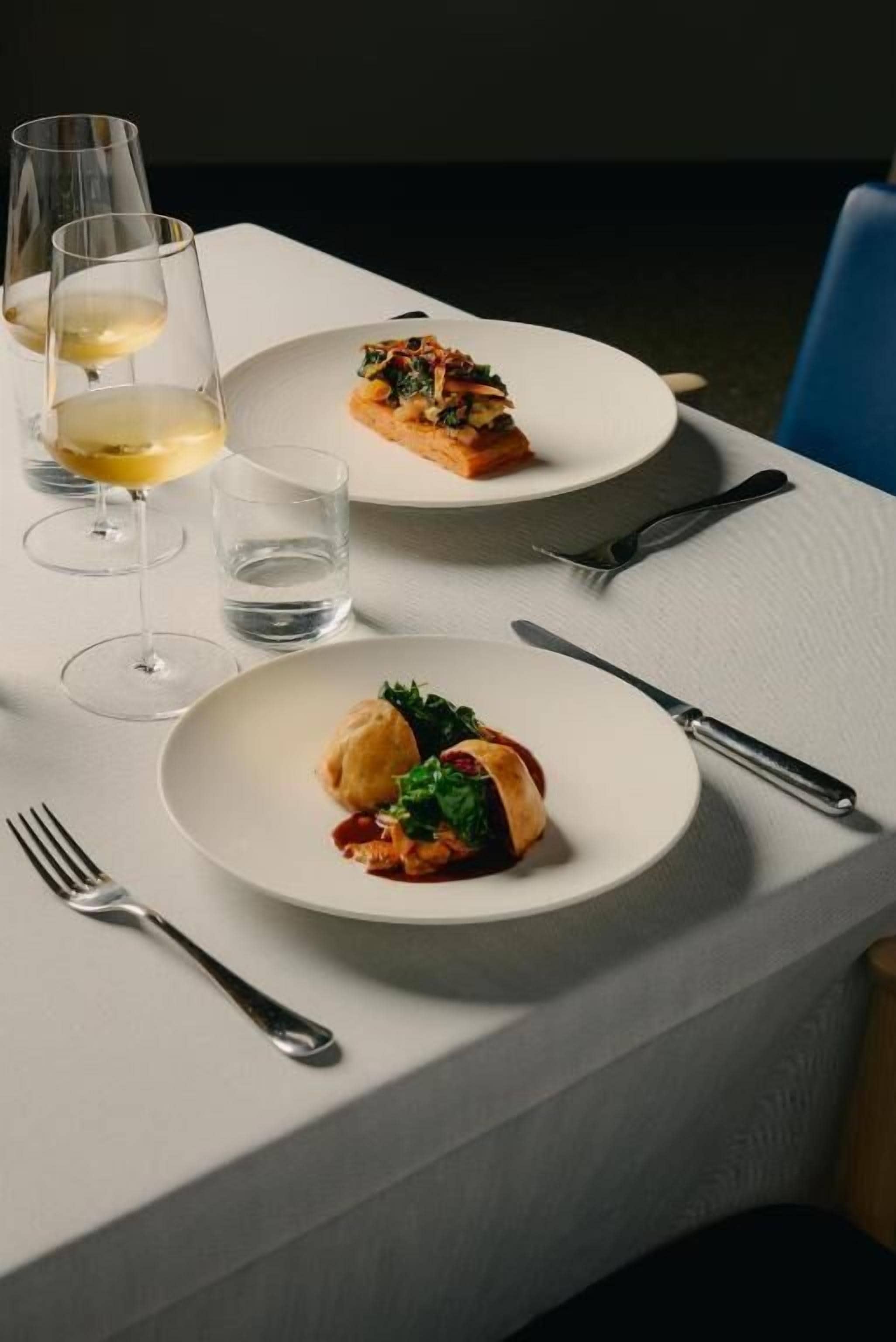 A table with two plates of food, a glass of white wine, and a glass of water.