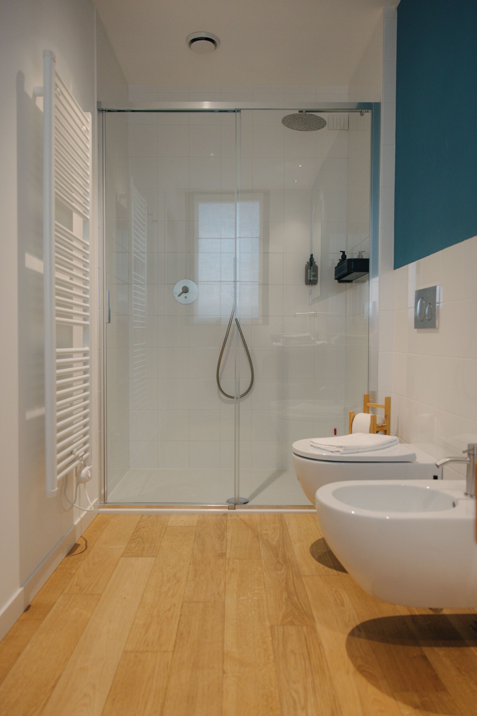 A modern bathroom with a glass shower enclosure, a white sink, and a wooden floor.