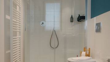A modern bathroom with a glass shower enclosure, a white sink, and a wooden floor.