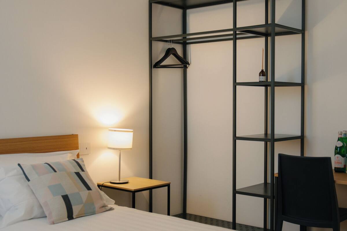 Ein Hotelzimmer mit Bett, Schreibtisch, Stuhl, Lampe und Kleiderschrank.