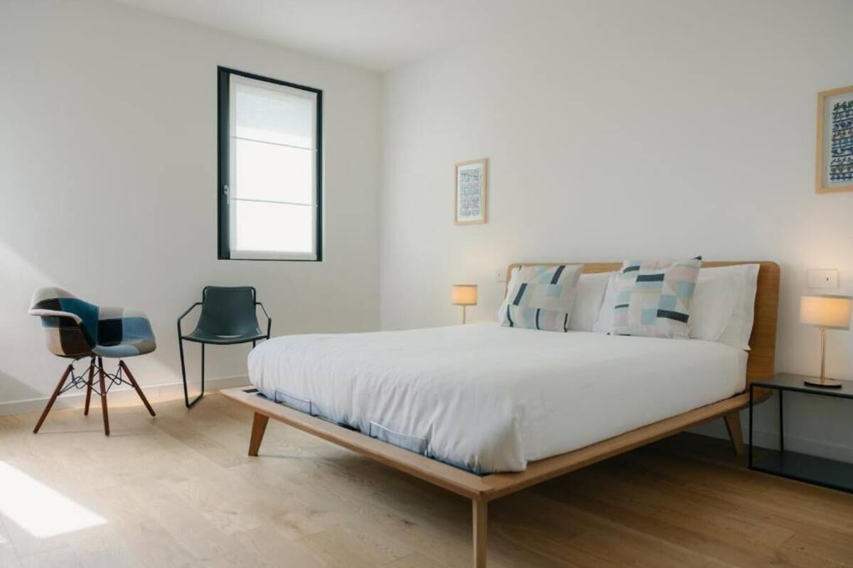 Ein Schlafzimmer mit einem Bett, zwei Stühlen, einem Fenster und einem Nachttisch.