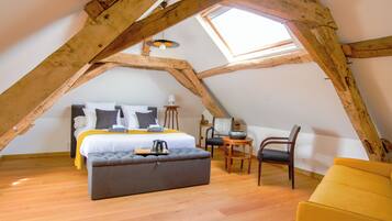 A loft bedroom with a sloped ceiling, a bed with pillows, a bedside table, a chair, and a small table with a lamp.