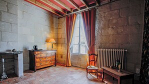 A room with a brick floor, a wooden dresser, a chair, a table, a radiator, and a window with curtains.