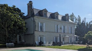 A rectangular swimming pool with a wooden deck, surrounded by a large building with multiple windows and a chimney.