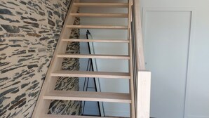 A wooden staircase with a handrail, leading to a room with a stone-patterned wall and a door.