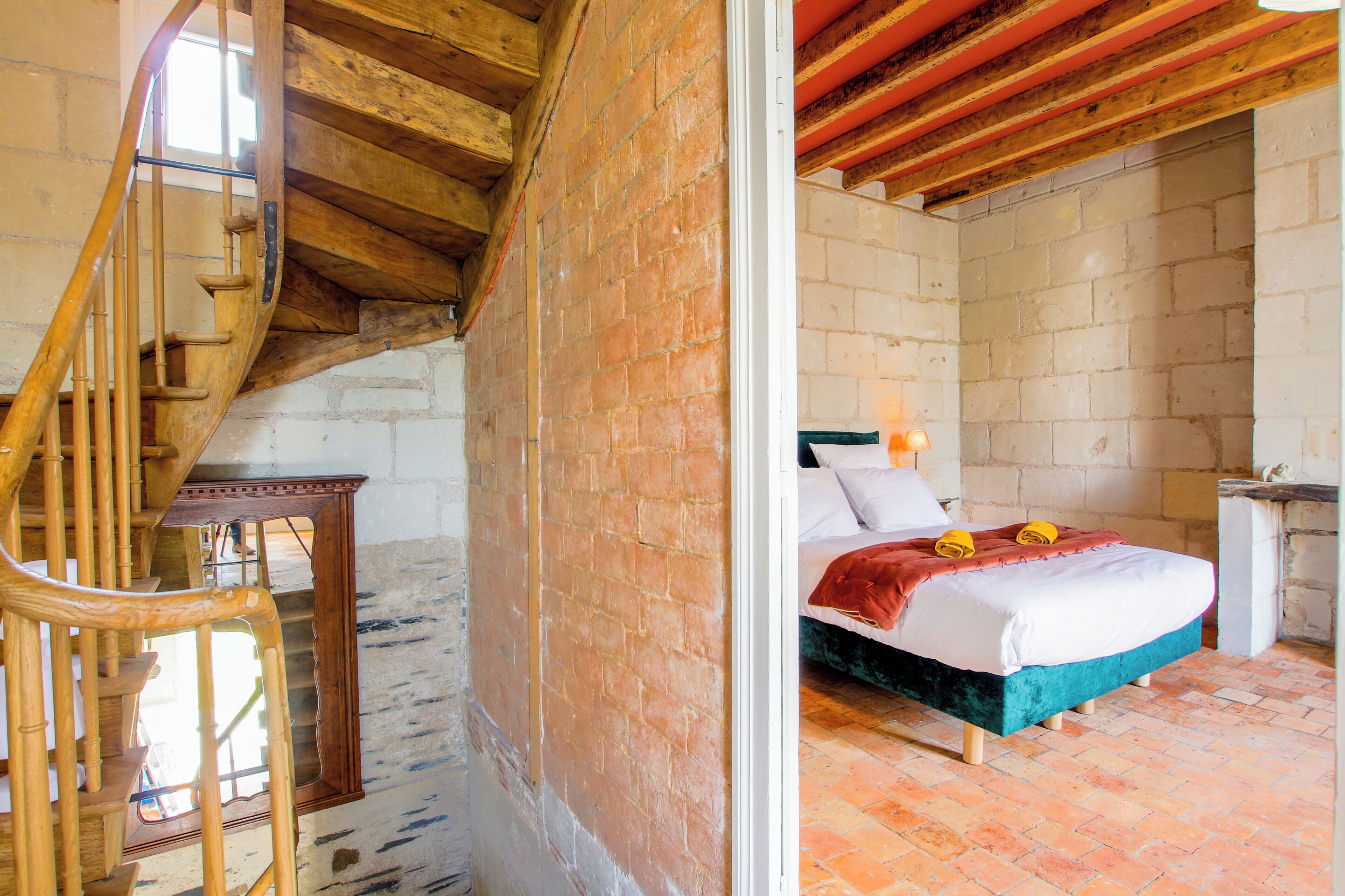 A bedroom with a wooden staircase, a brick wall, and a bed with a red blanket.