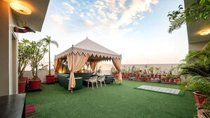 A covered outdoor seating area with a table and chairs, surrounded by potted plants.