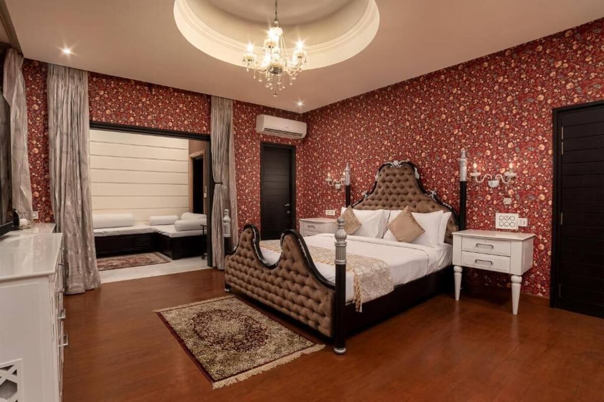 Un dormitorio con una cama grande, una araña, una mesita de noche y un papel tapiz floral rojo.