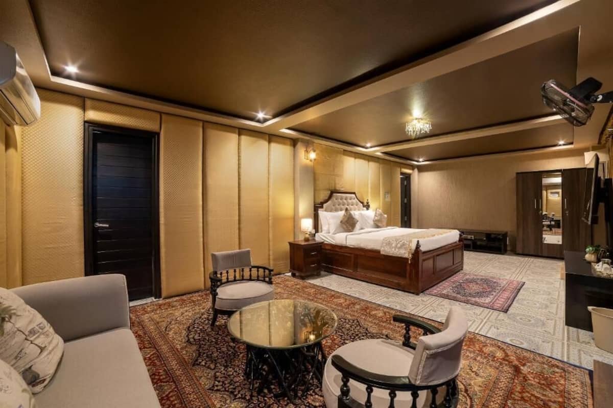 Una habitación de hotel con una cama grande, dos sillas, una mesita y una araña.