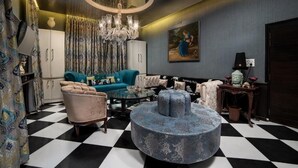 A living room with a checkered floor, a round blue ottoman, a blue sofa, a chandelier, and a Buddha statue.