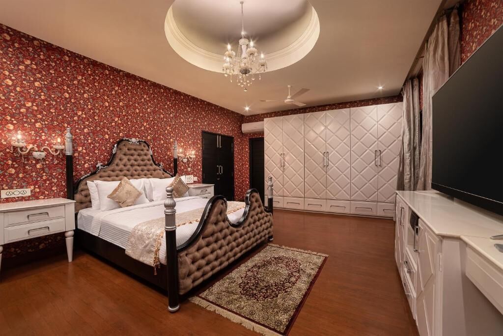 A bedroom with a large bed, a chandelier, a TV, and a wardrobe.