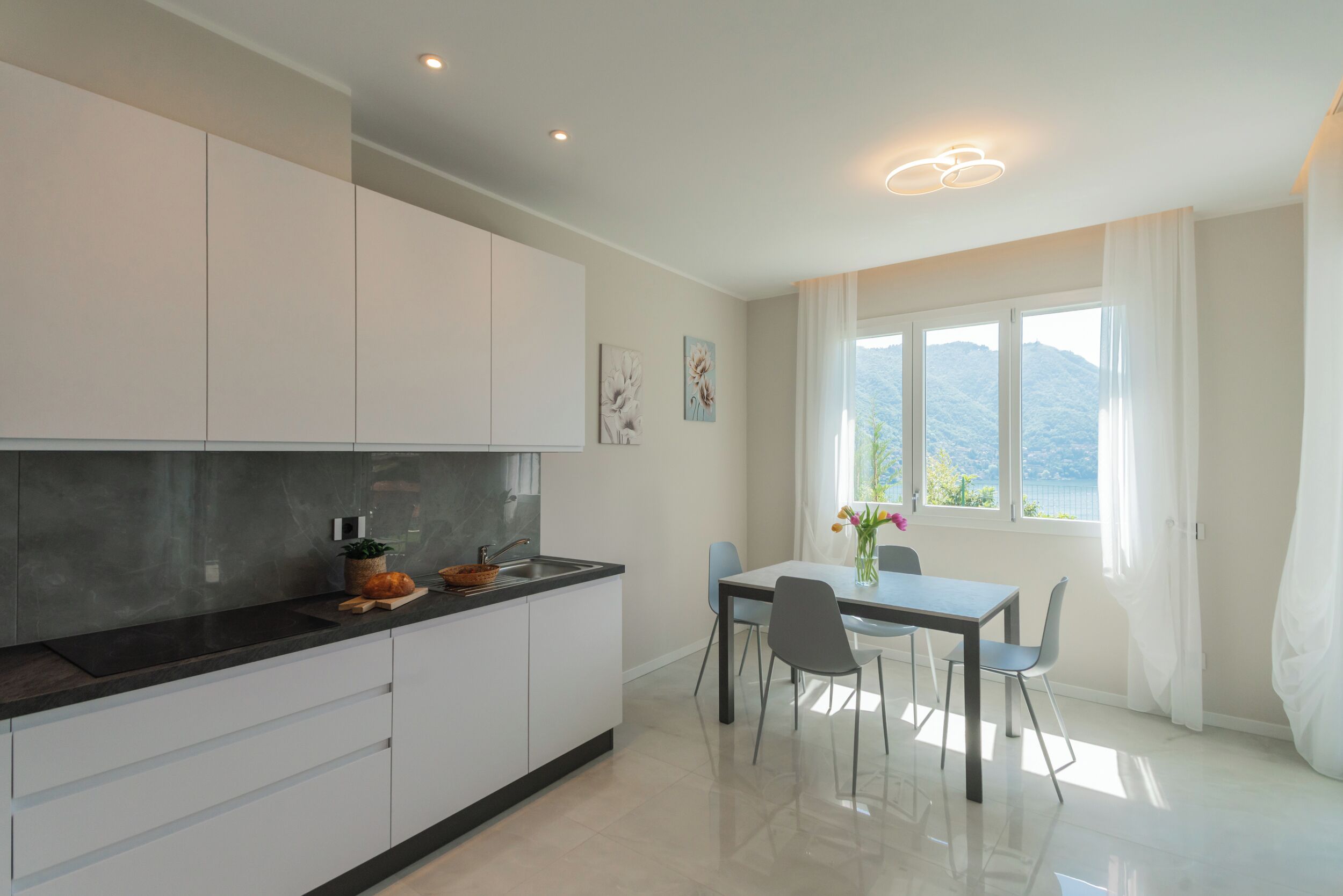 Une cuisine moderne avec des meubles blancs, un plan de travail noir et un coin repas comprenant une table et des chaises.