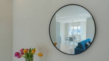 A round mirror on a wall, reflecting a room with a blue sofa, a dining table, and chairs.