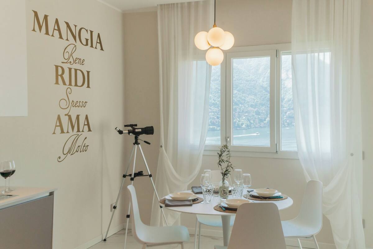 A dining area with a table set for two, a tripod-mounted camera, and a view of the city through a window.
