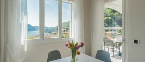 A dining area with a table and chairs, a vase with flowers, and a view of a mountainous landscape through large windows.