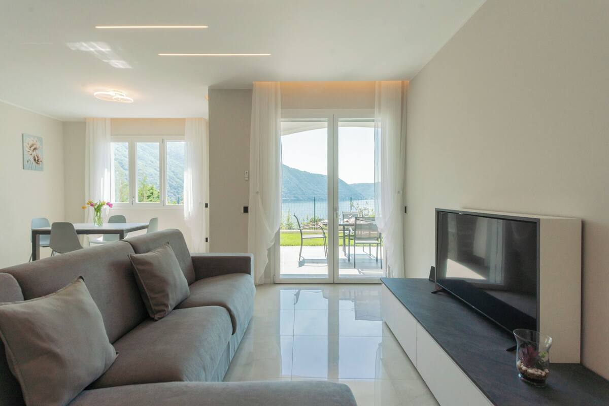 A modern living room with a sofa, a flat-screen TV, and a glass table.