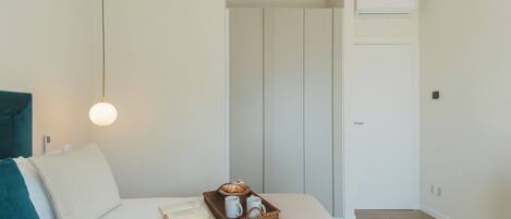 Un dormitorio con cama, una mesita de noche, una bandeja con un croissant y un aire acondicionado de pared.