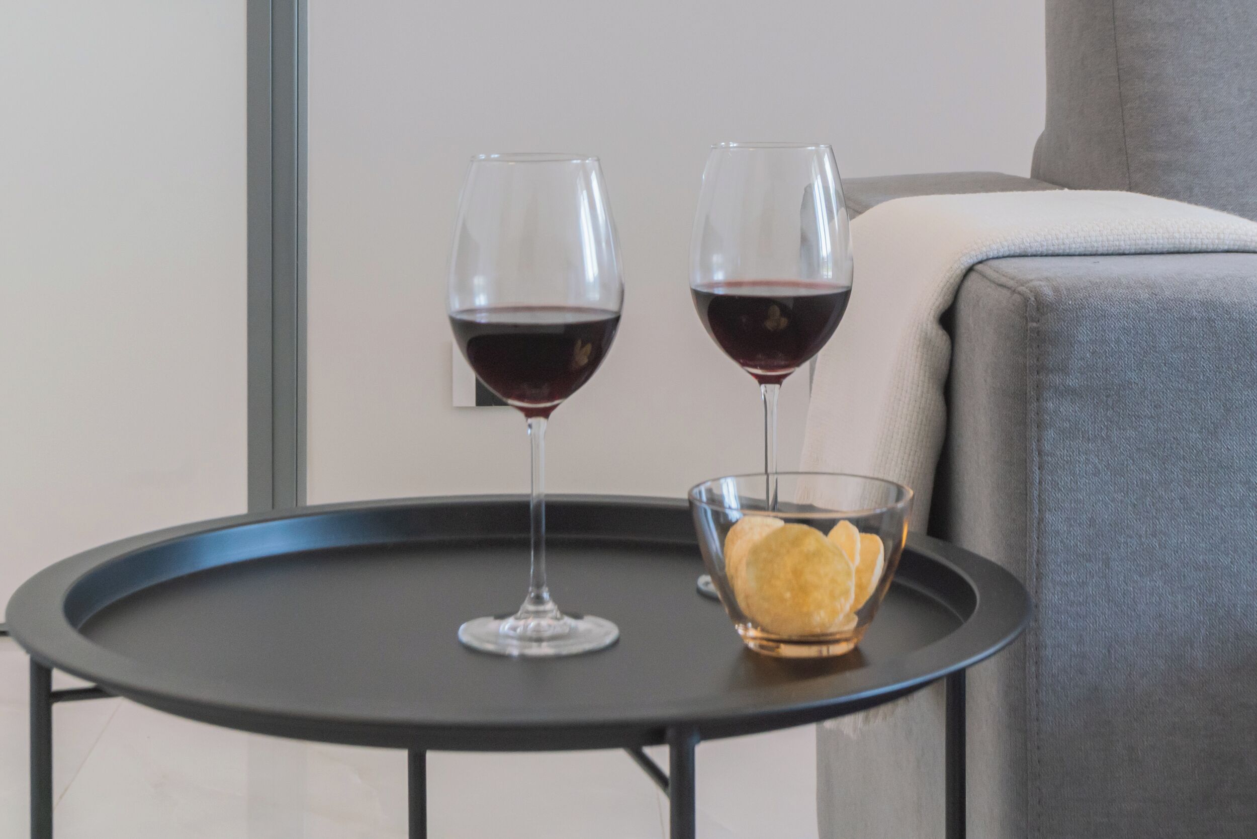 Mesa redonda com duas taças de vinho e um recipiente com petiscos.