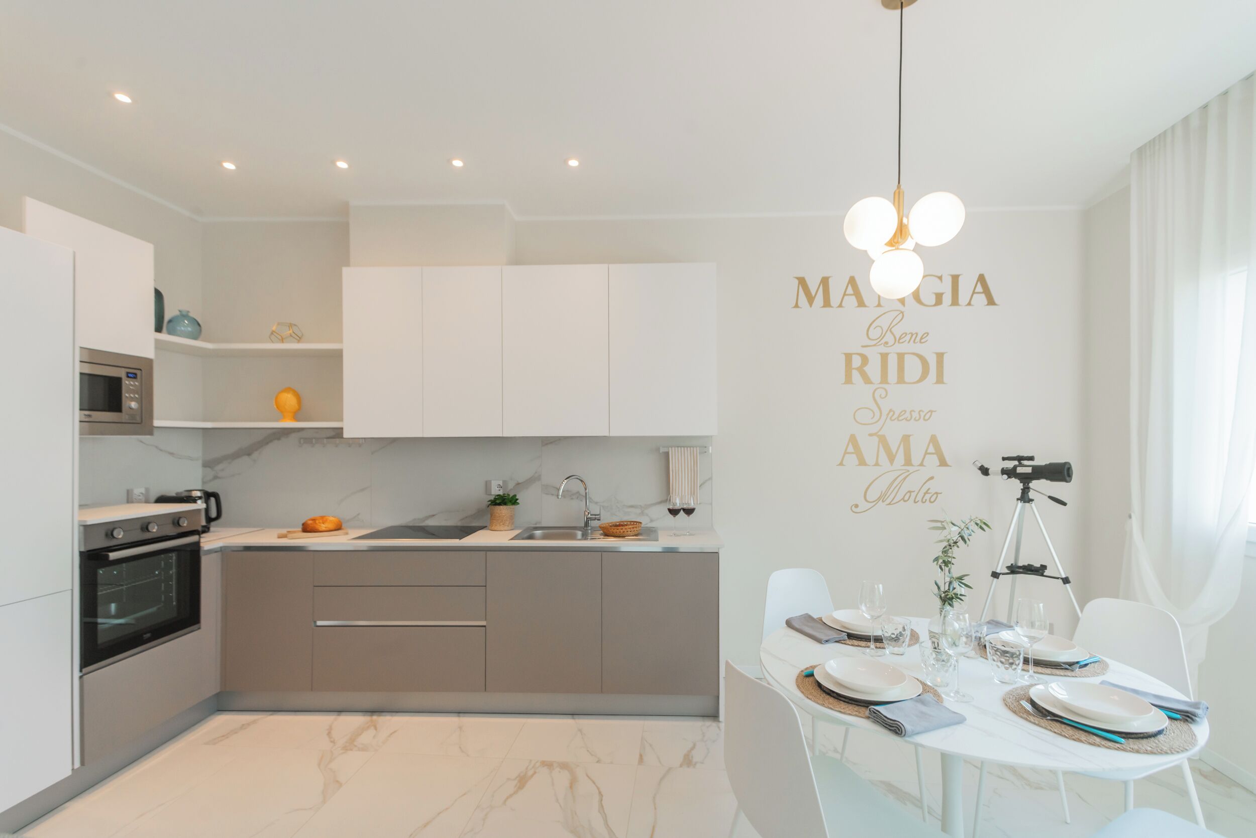 A modern kitchen with a built-in oven, a sink, and a dining area with a table set for two.